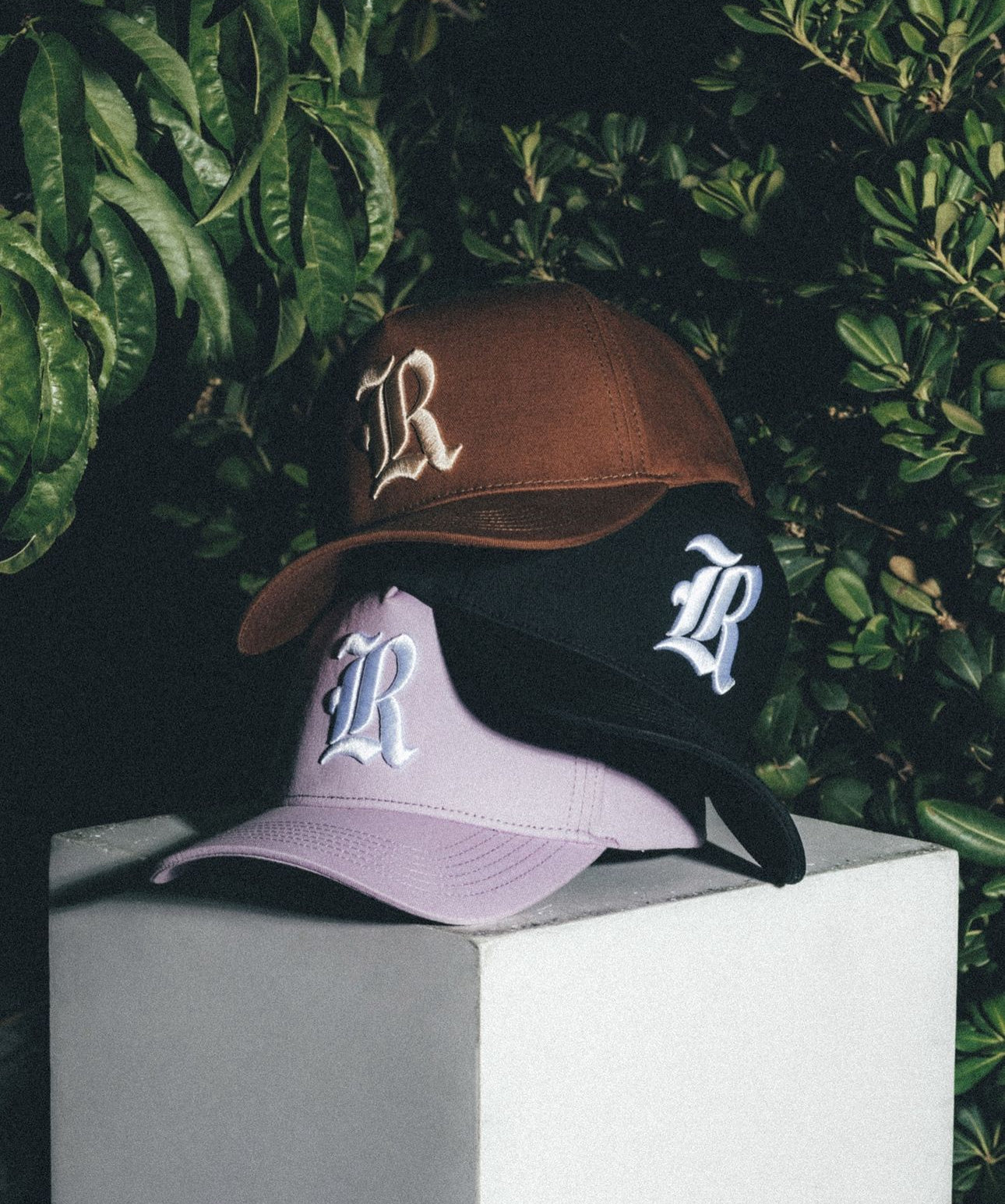 Three custom embroidered hats produced by Waves: brown, black and lavender hats photographed against greenery